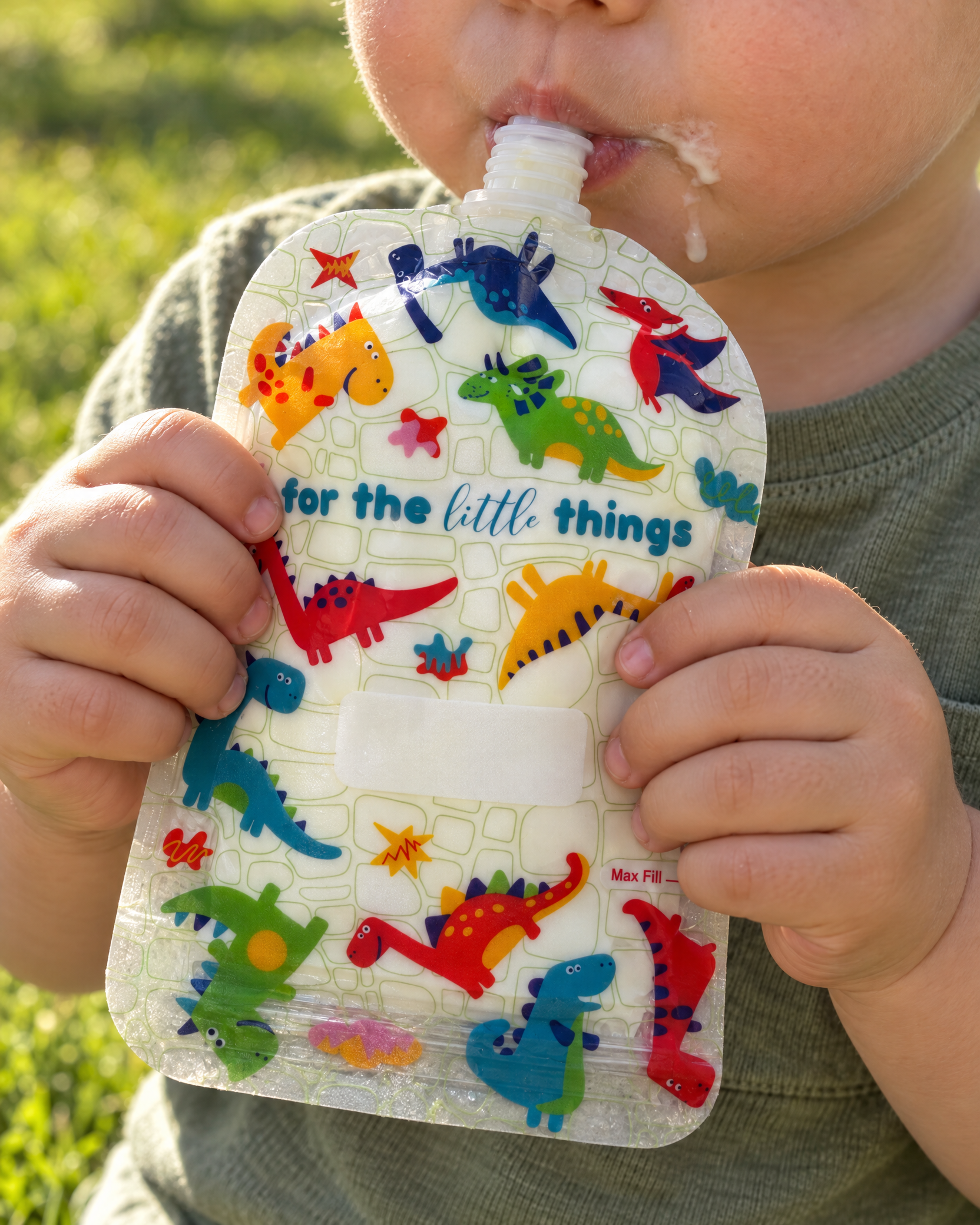 Toddler drinking from a dinosaur print reusable food pouch