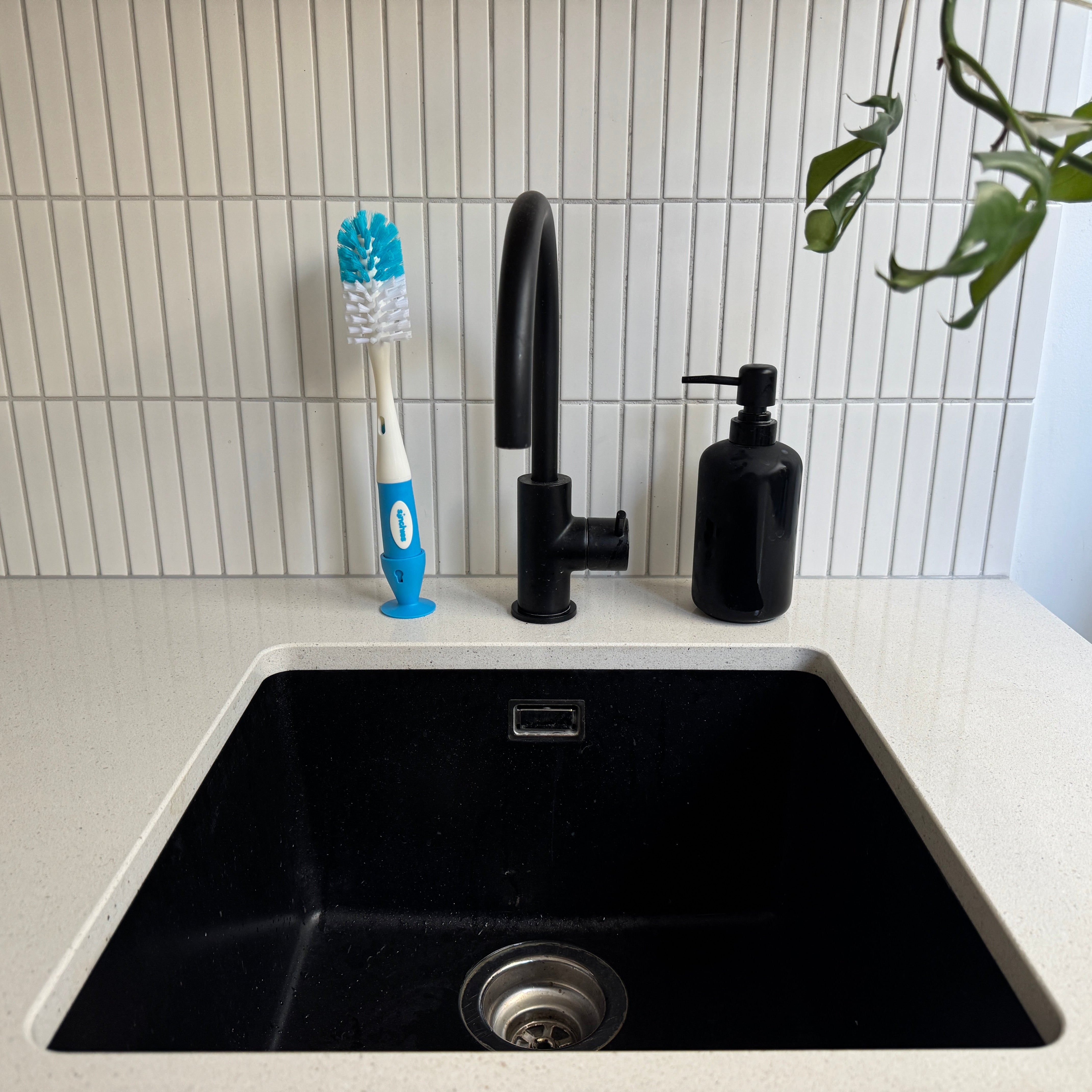 Black kitchen sink with a black faucet and soap dispenser on a white tiled wall.