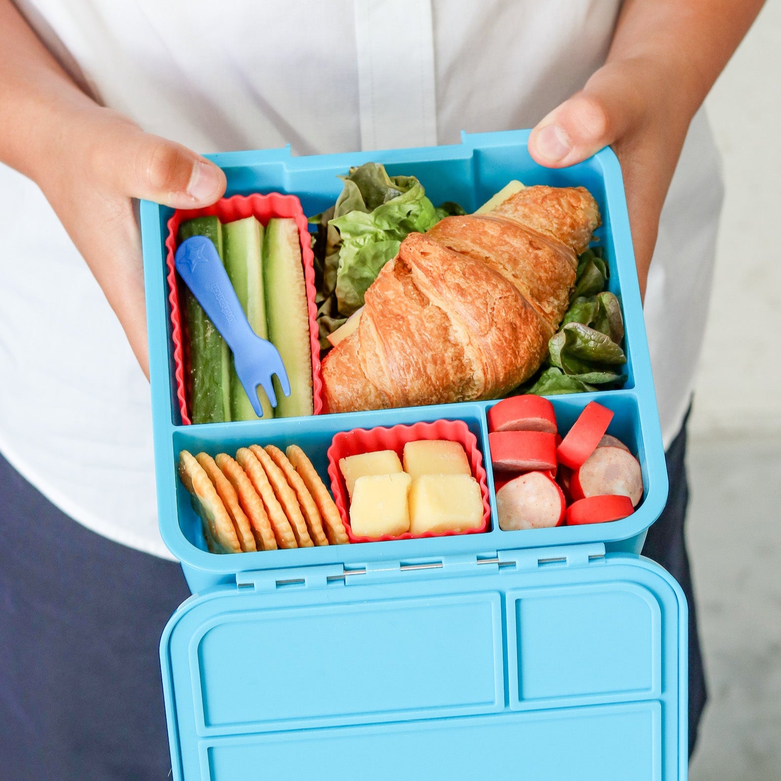 Blue bento box filled with a variety of food items held by a person.