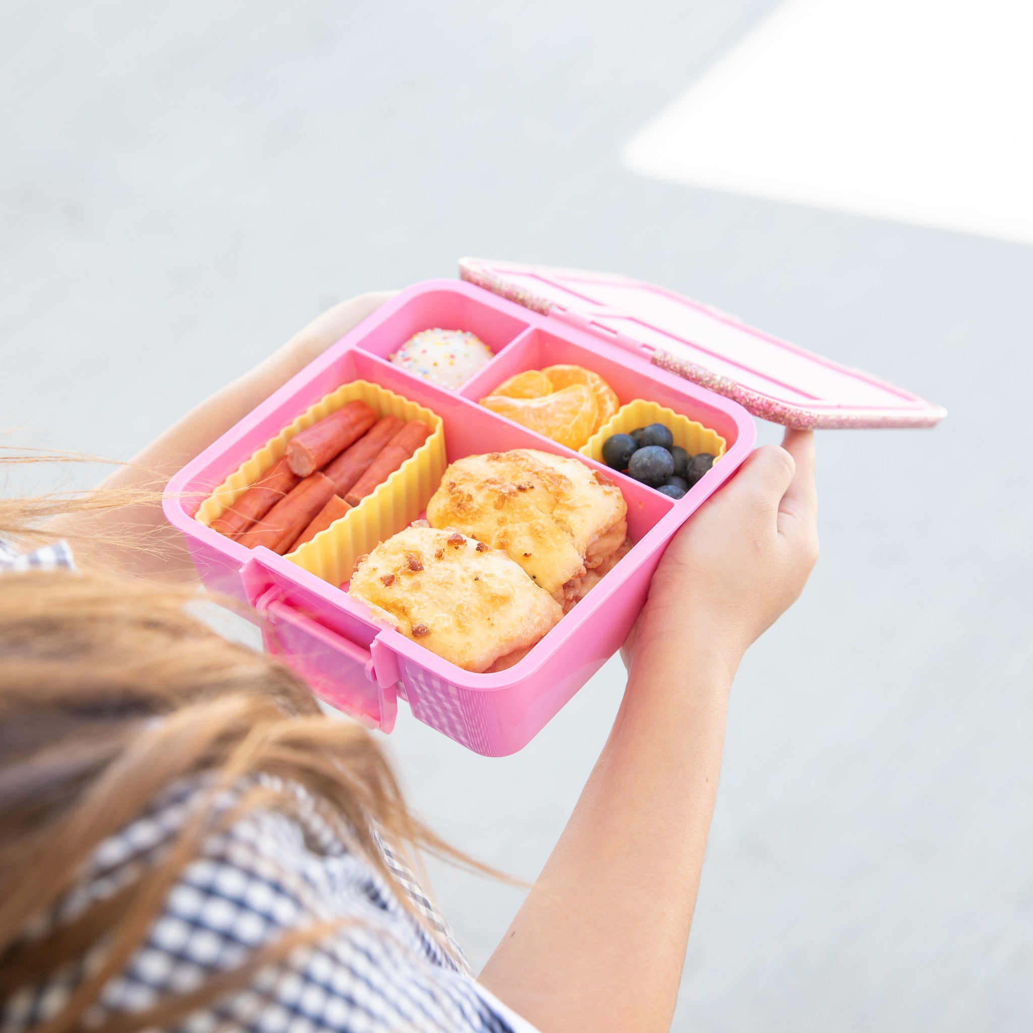 Person holding a pink bento box with compartments of food against a light background
