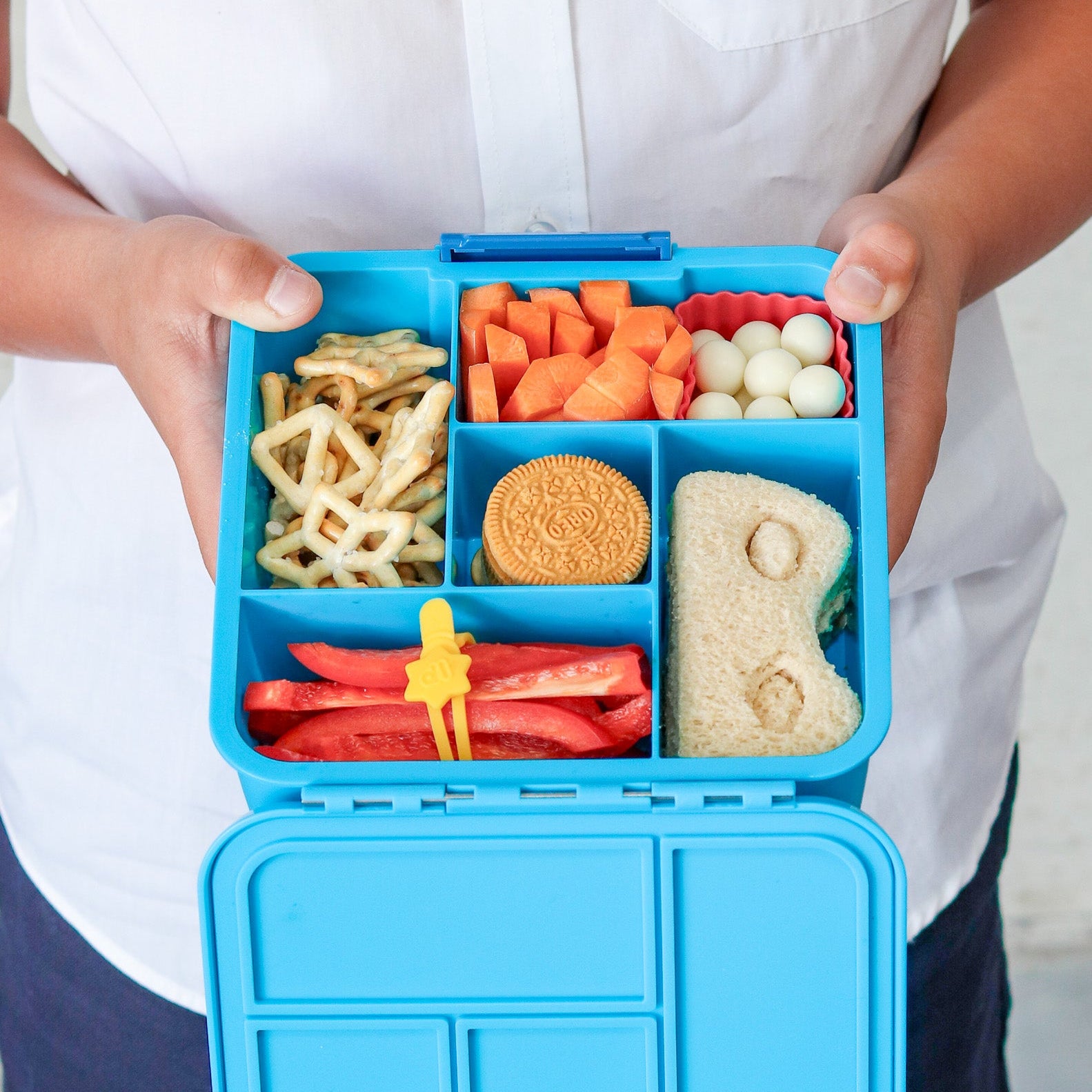 Blue bento box filled with various snacks held by a person wearing a white shirt.