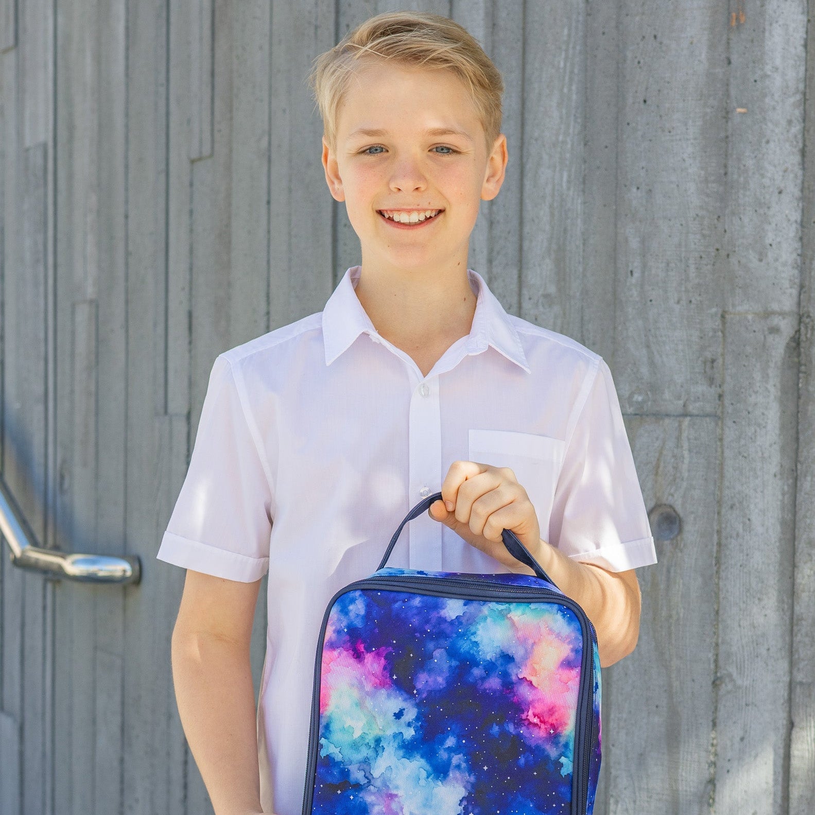 Young boy holding a colorful backpack against a wooden background