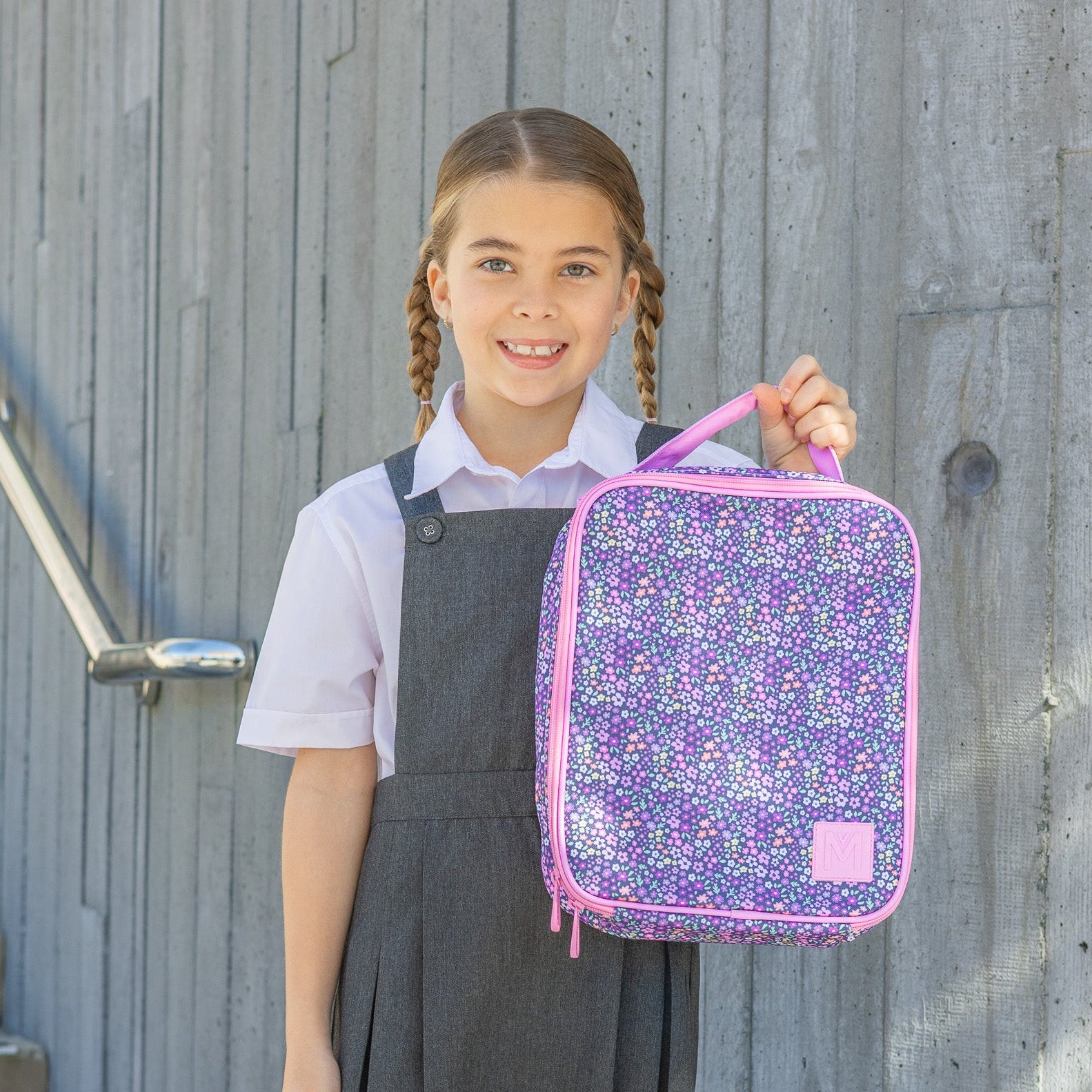 Girl holding a floral patterned lunch bag against a wooden background