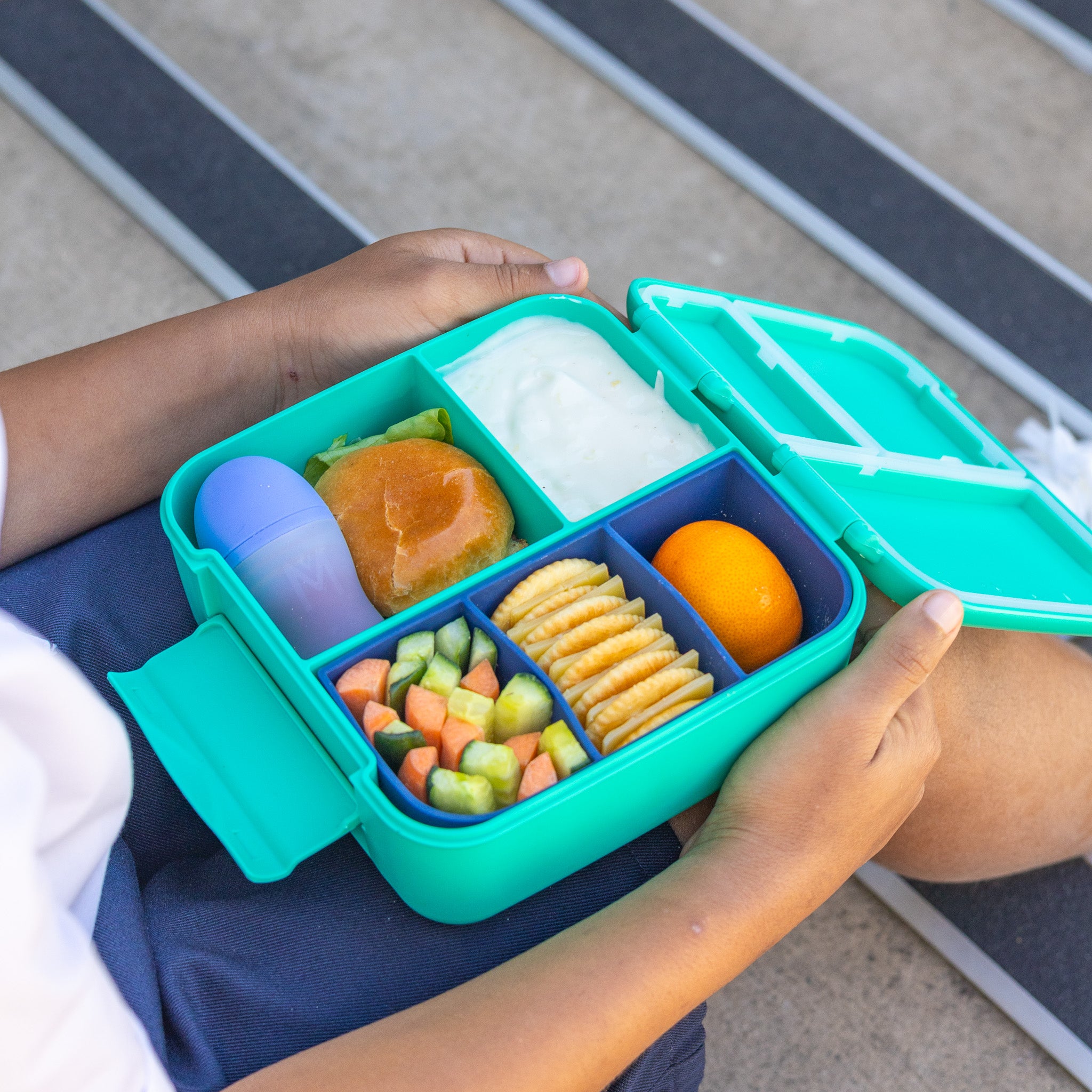 Person holding a teal bento box with compartments of food