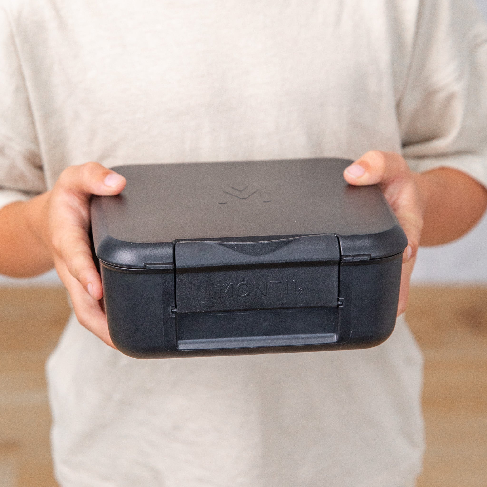 Person holding a black lunch box with 'Montii' branding.