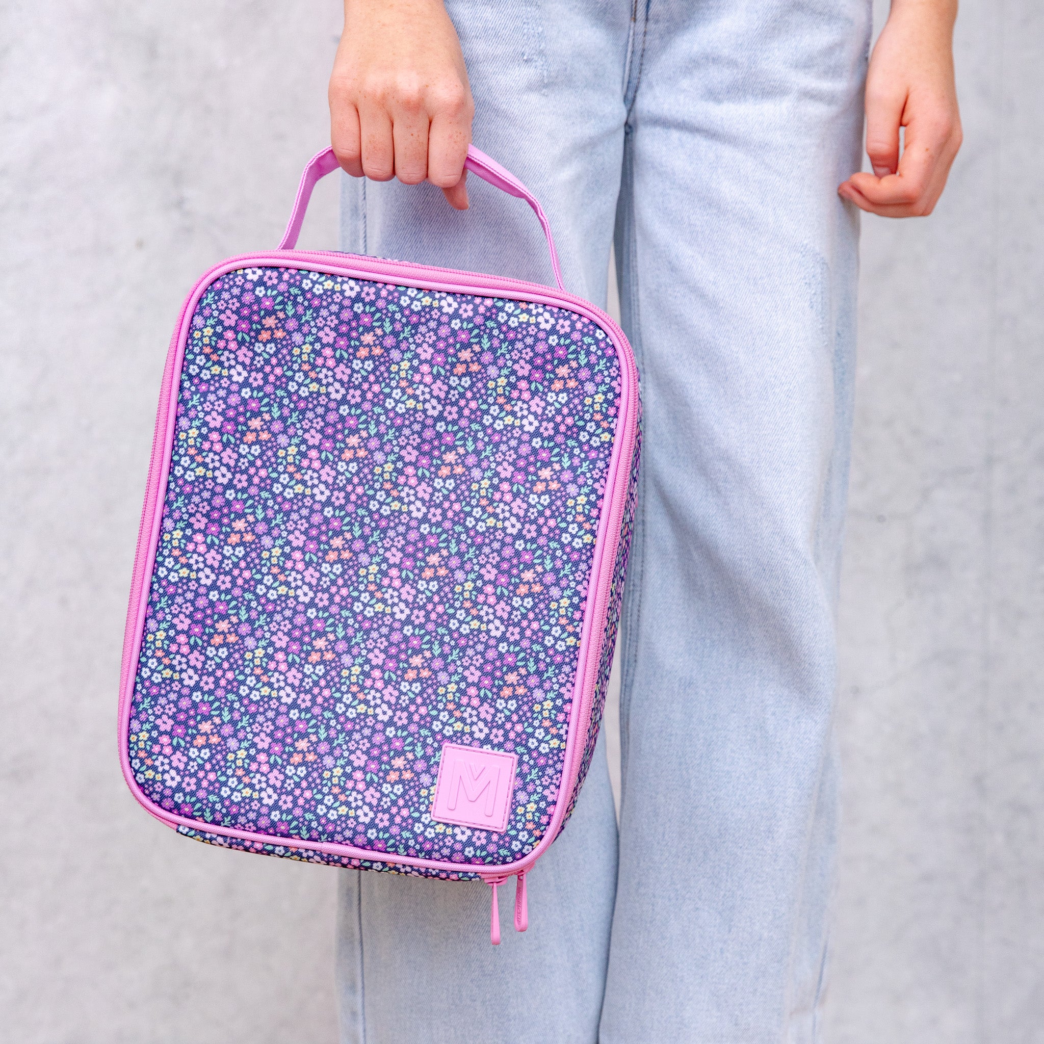 Person holding a floral-patterned lunch bag with pink trim against a plain background