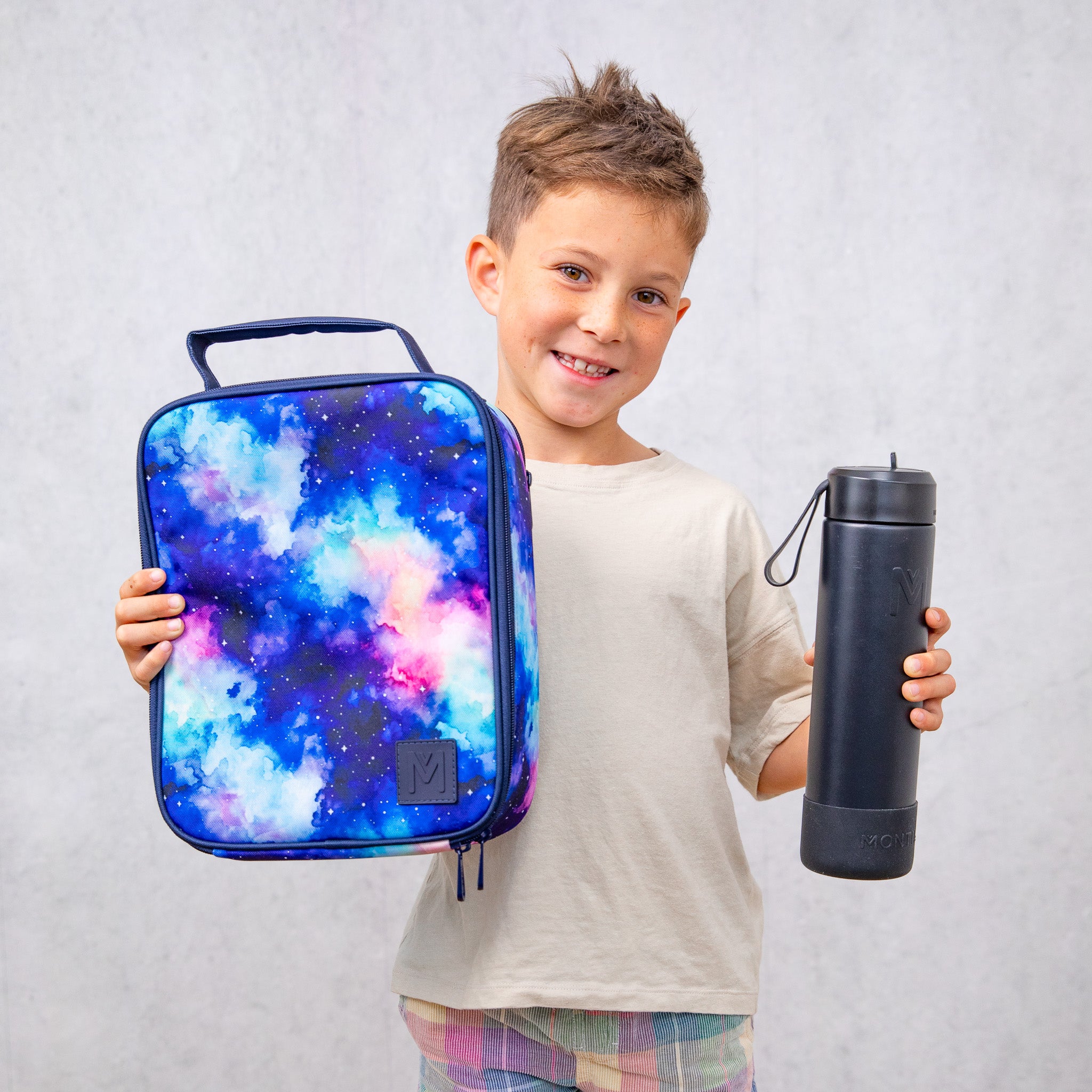 Child holding a colorful insulated lunch bag and a black water bottle against a plain background