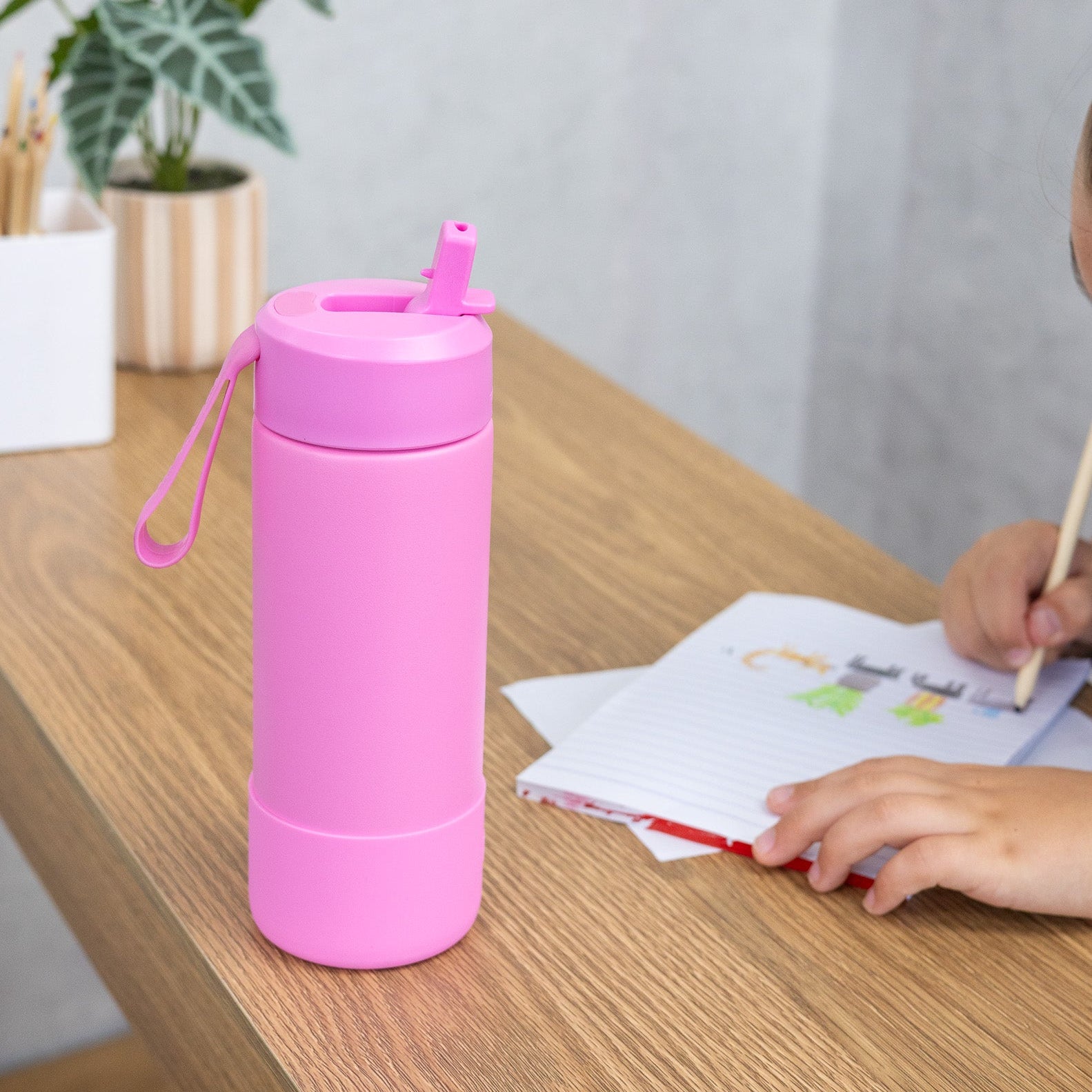 Pink water bottle on a wooden desk with a person writing in the background