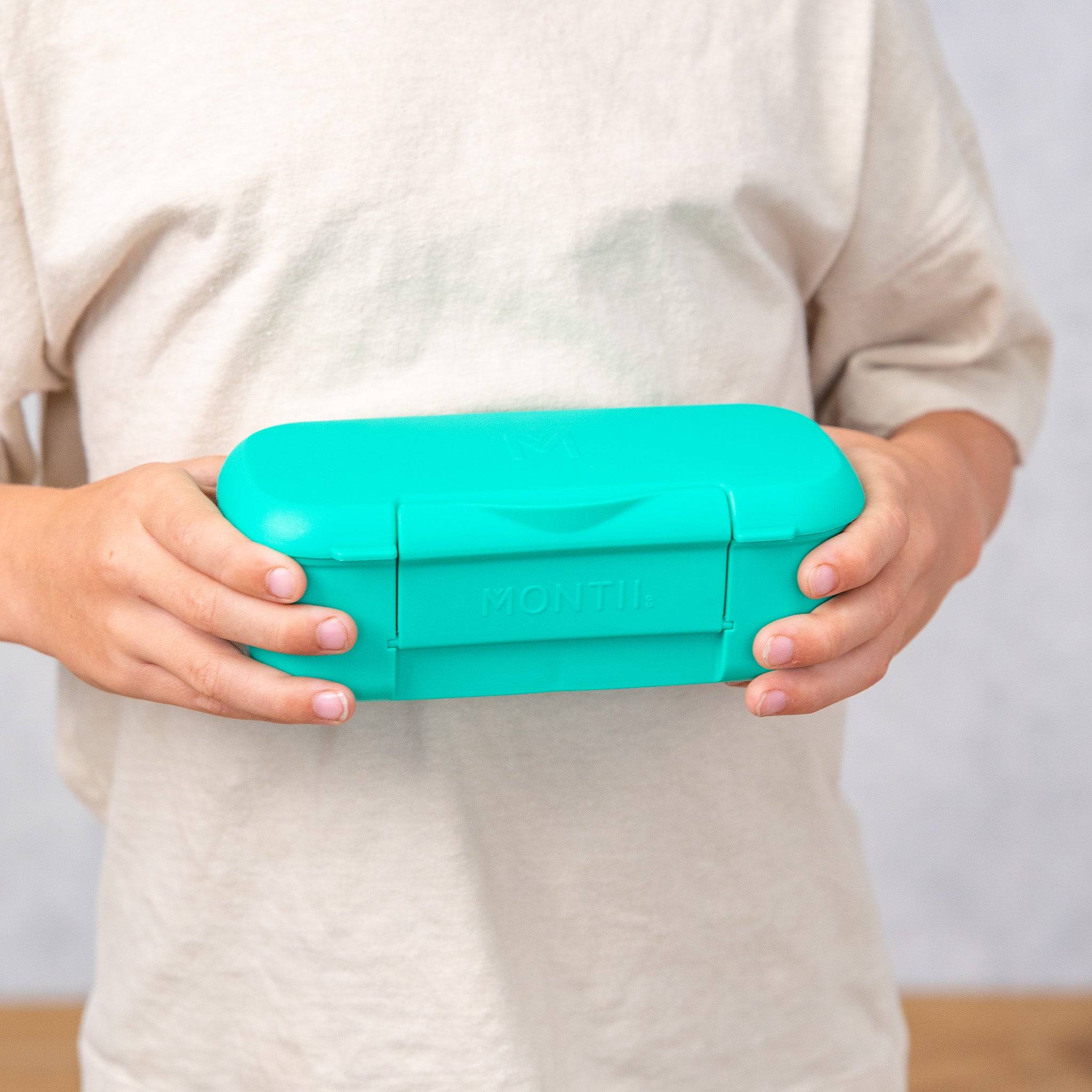 Person holding a teal lunch box with a plain background