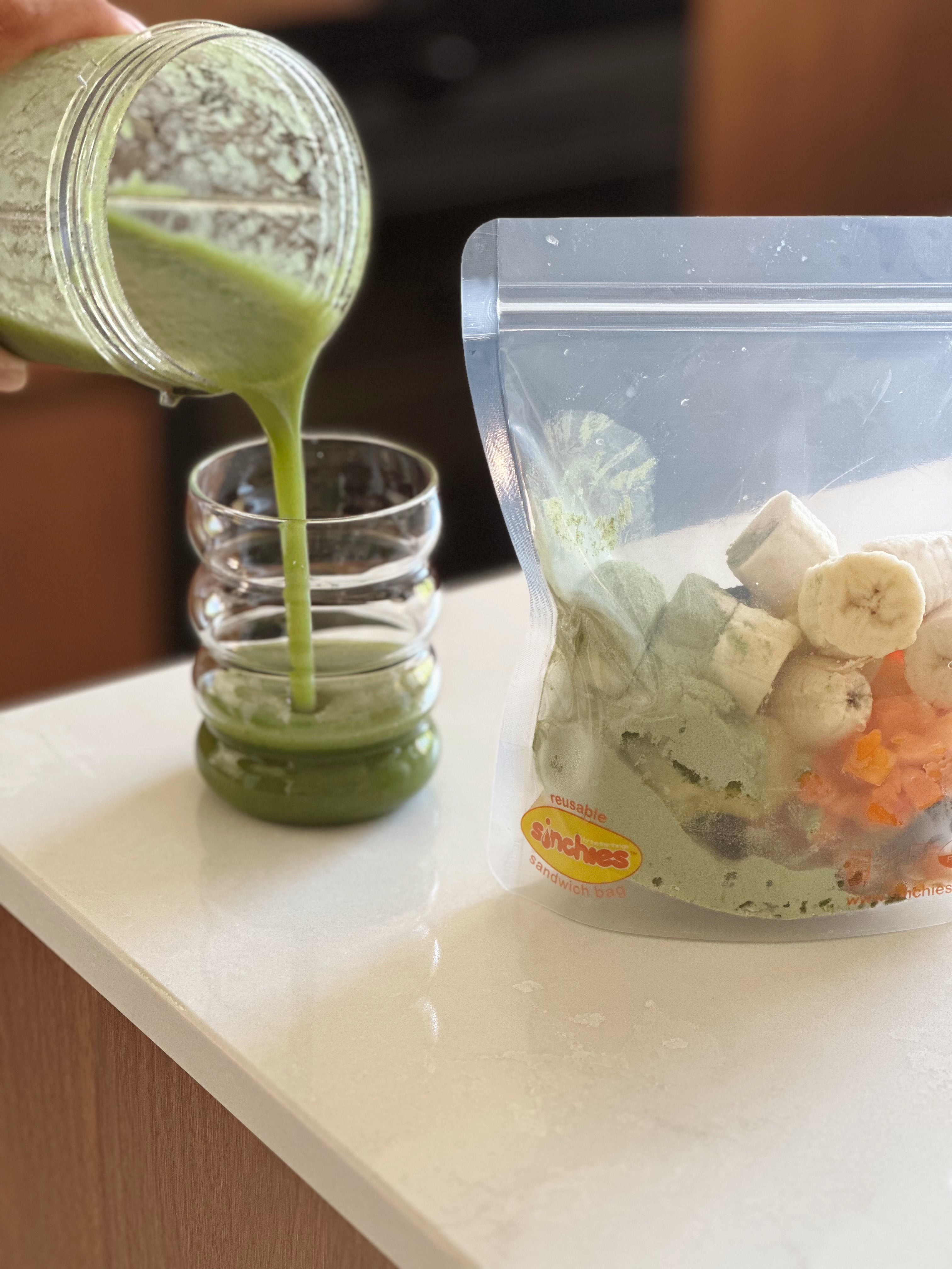 Green smoothie being poured into a glass with a bag of ingredients on a counter.