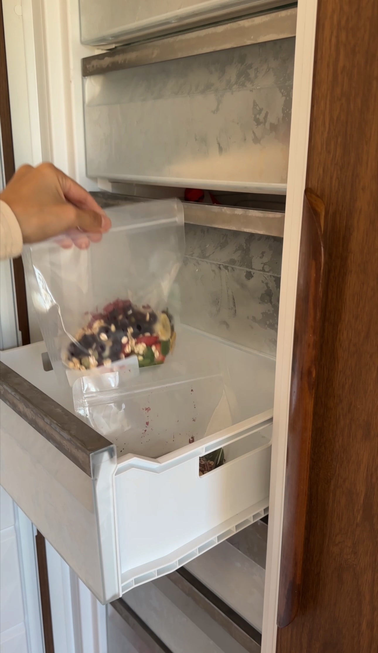 Person reaching into an open refrigerator with a bag of snacks.