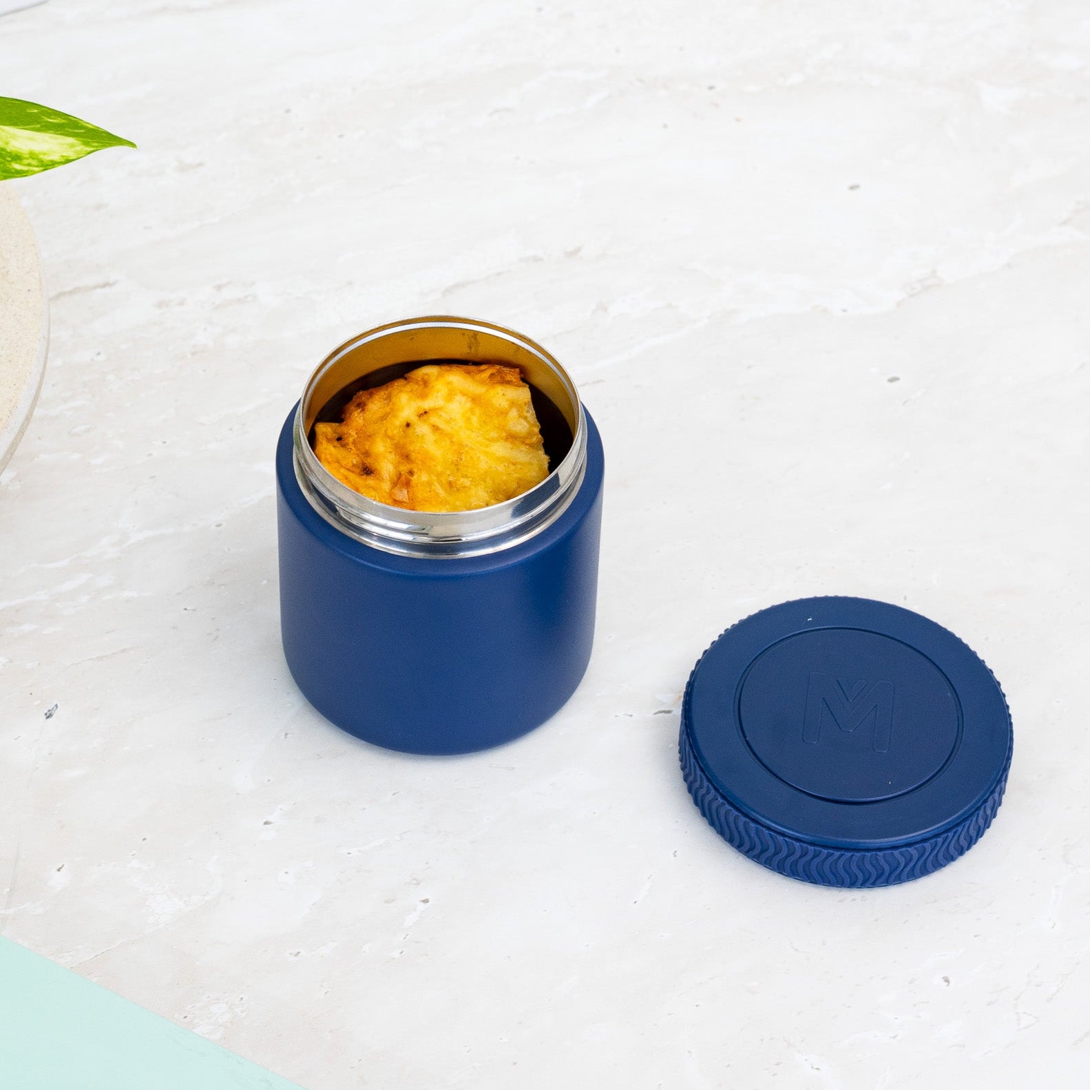 Blue insulated food container with food inside on a light surface